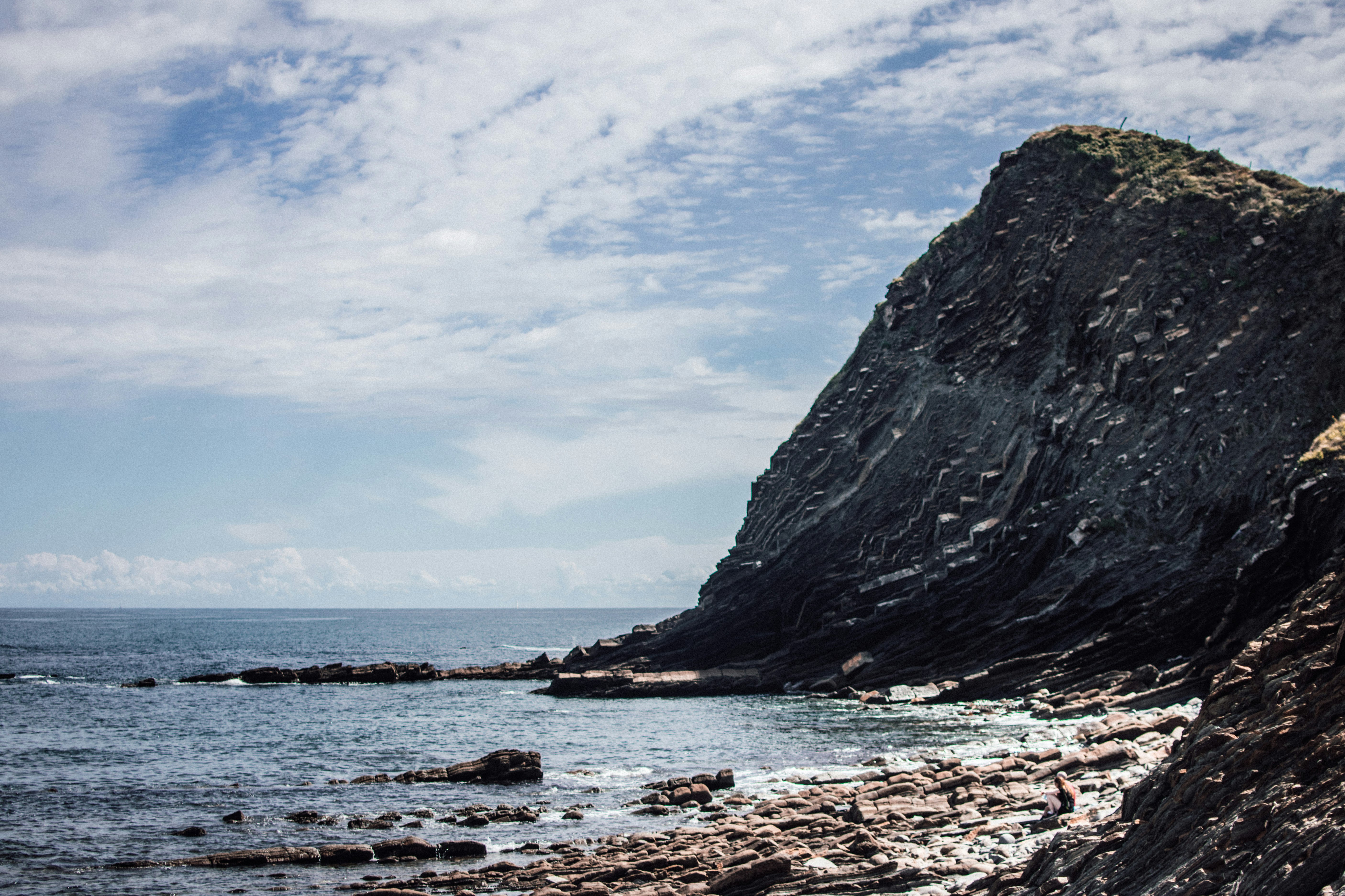 black rock formation on sea under white clouds and blue sky during daytime